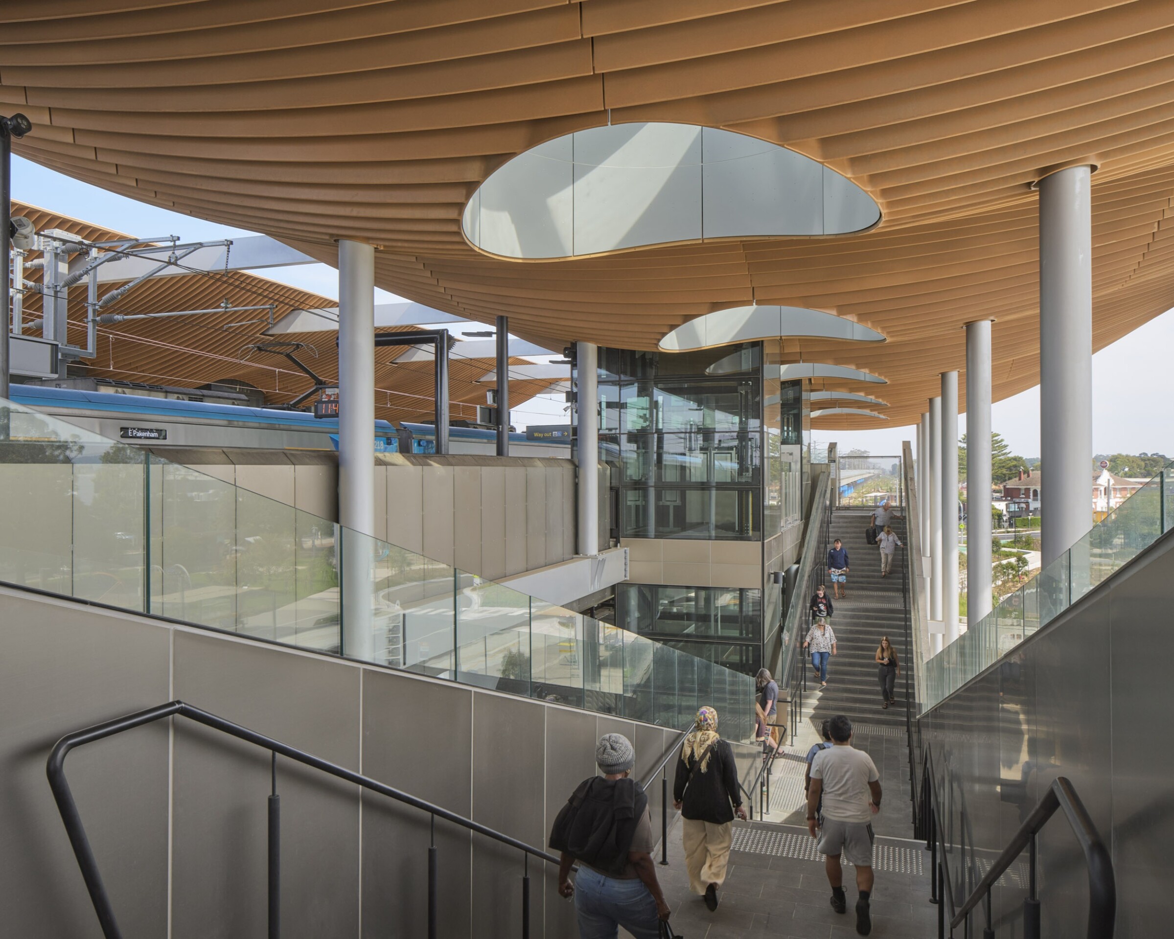 Passengers moving through a contemporary train station with canopy, glass lifts and stairs, designed by Genton to showcase aviation and transport interchange expertise